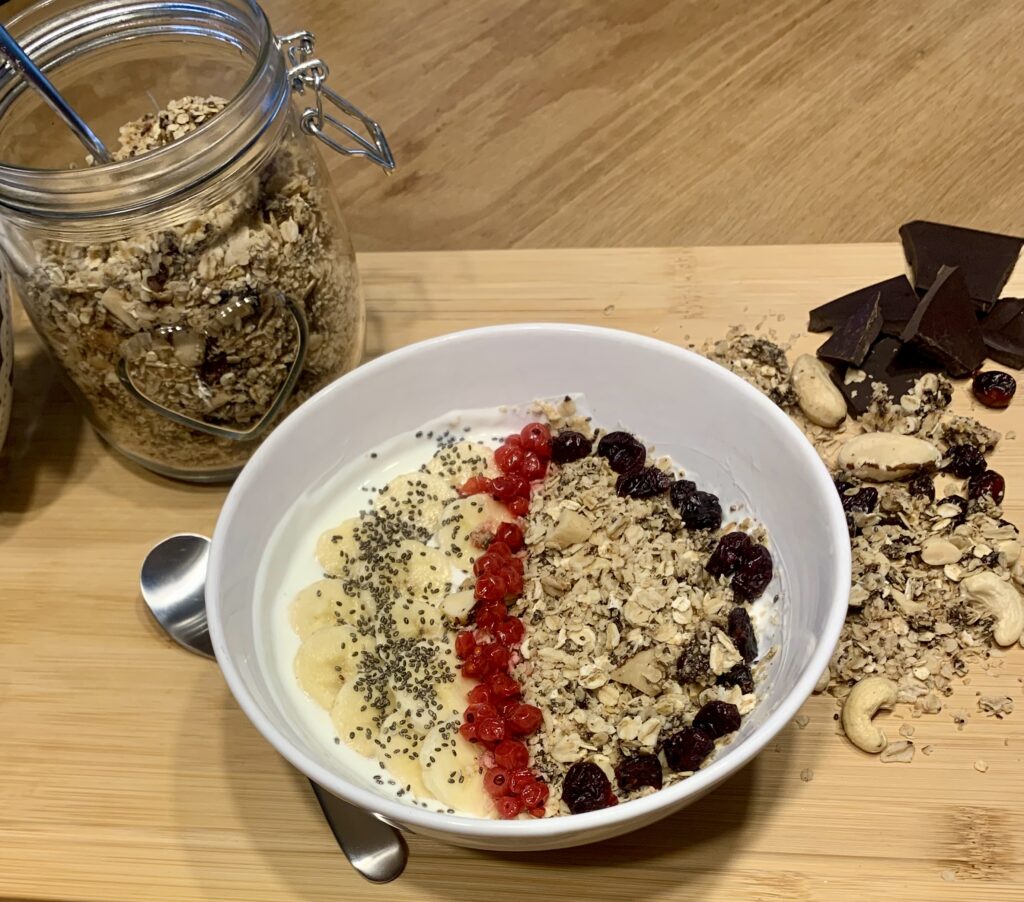 V bílé misce nandaná domácí granola sestávající z ovesných vloček, směsi ořechů, chia semínek, brusinek a rozinek.